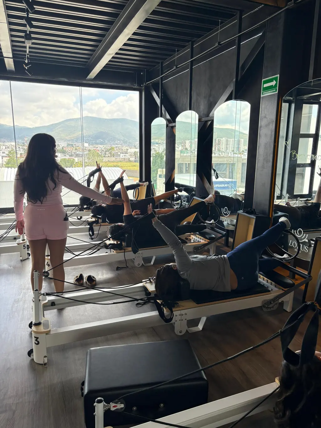 Clase de Pilates Reformer en curso con coach acompañando, luz de día